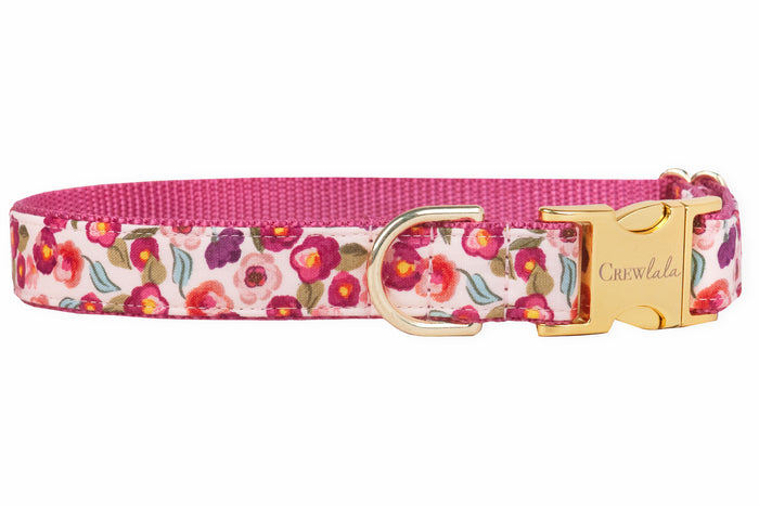 Bright floral dog collar made from fabric patterned with miniature pink blooms. The strap has a dark pink woven backing for durability, and metal hardware, including a D-ring and engraved buckle.