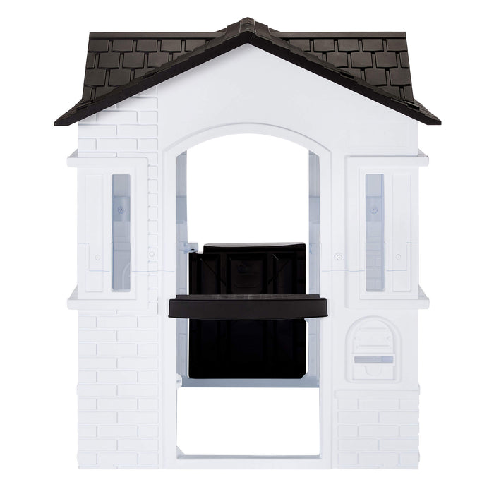 A white plastic playhouse with a black tiled roof featuring an open back with a mail slot isolated on a white background.