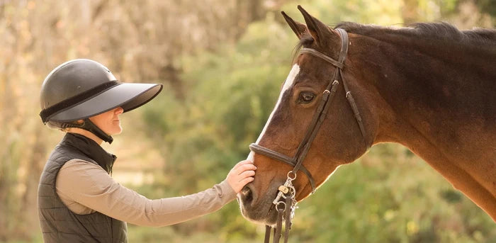 Person in equestrian gear interacting with a horse outdoors
