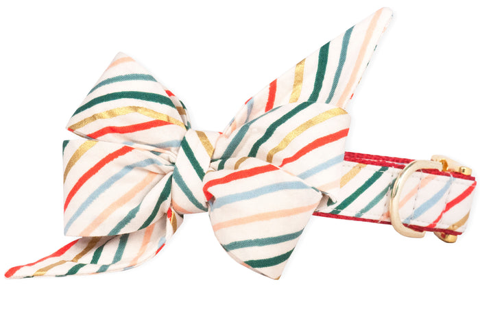 Festive dog collar showcasing an oversized feminine belle bow. The cream background is patterned with diagonal stripes in emerald, crimson, metallic gold, light blue, and blush, attached to a collar with red edging and gold hardware.