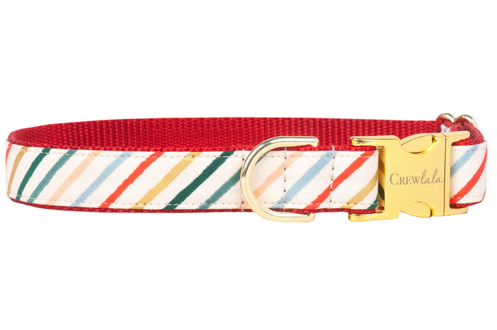 A festive dog collar with diagonal holiday stripes in red, green, gold, blush, and light blue on a cream background. The collar is finished with a dark green backing and shiny gold hardware.