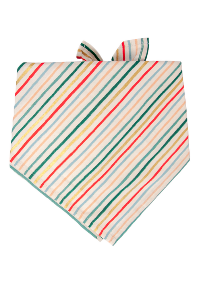 A holiday bandana for dogs, designed with diagonal stripes in vibrant seasonal colors: red, green, metallic gold, pastel blue, and peach. The cream background highlights the playful, festive design.