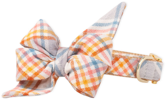 Pastel plaid dog collar with a large, statement belle bow attached at the front. The flannel fabric has intersecting lines in soft shades. The collar includes a metal D-ring and buckle, blending fashion with function.