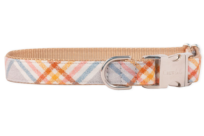 A dog collar made of soft flannel pastel plaid fabric featuring diagonal stripes. The collar has a tan nylon backing, a metal D-ring for leash attachment, and metal side-release buckle engraved with the brand name “Crewlala.”